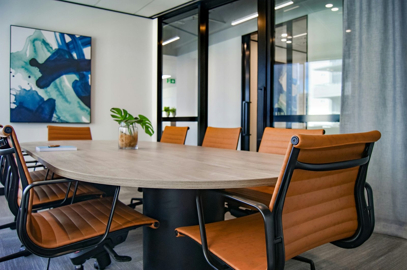 A clean, professional commercial meeting room with a wooden conference table, leather chairs, and modern artwork
